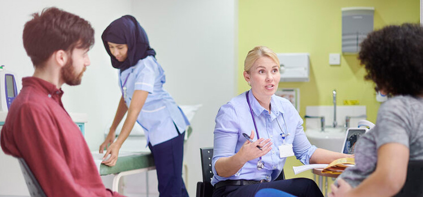 Female doctor chatting with pregant woman with a nurse and man looking on